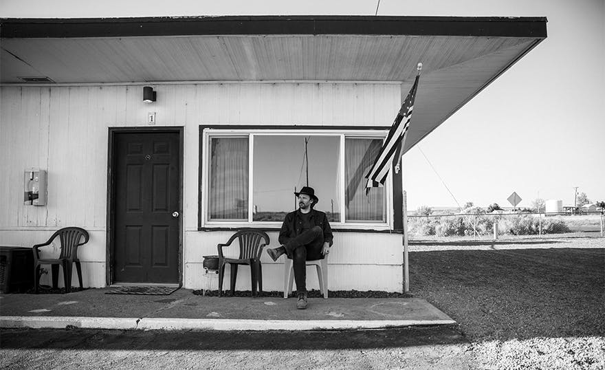 A portrait of Joe Day sitting in front of an old motel in the Washington desert.