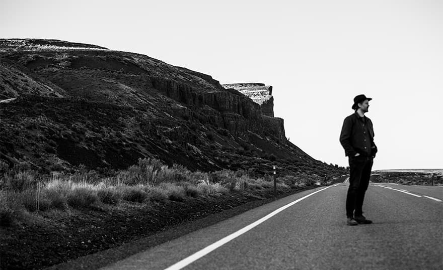 A portrait of Joe Day leaning against a broken down school house in Govan, WA